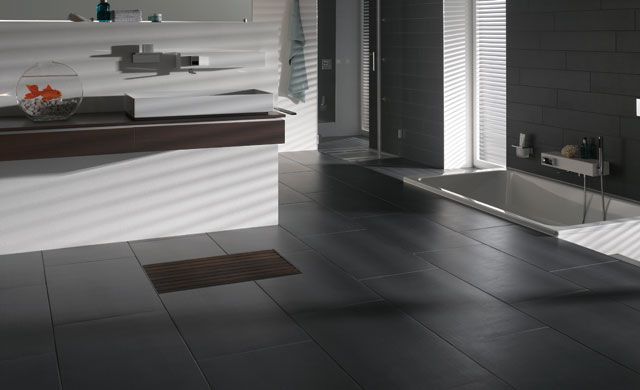 Modernes Badezimmer mit dunklen Strukturfliesen, Badewanne, Waschtisch und Goldfischglas auf der Ablage.